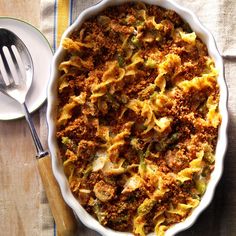 a casserole dish with meat and vegetables in it on a wooden table next to a spoon