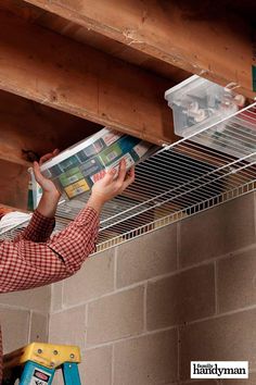 a man reading a magazine while hanging from a ceiling rack on a brick wall above a ladder