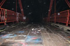 an old wooden bridge with graffiti on the sides and metal railings at night time