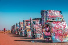 an old car covered in graffiti sitting on the side of a dirt road