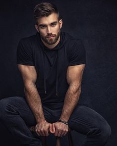 a man sitting on top of a stool with his hands in his pockets and looking at the camera