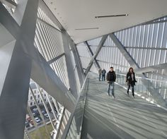 people are walking on the walkway in an indoor area with glass walls and metal railings