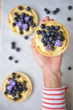 a person holding up a pastry with blueberries on it and flowers in the middle