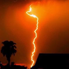 a lightning bolt is seen in the sky over a house and palm tree at night