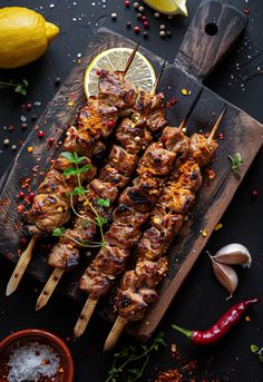 skewers of meat and vegetables on a wooden cutting board with lemons, peppercorst, salt and pepper sprinkles