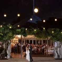 a bride and groom dance under the lights at their wedding reception in an outdoor venue