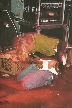 a young man playing an electric guitar in front of some other guitars and amps