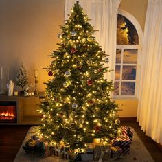 a lit christmas tree in a living room with presents under it and stockings on the floor