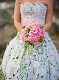 a woman in a white dress holding a bouquet of pink hydrangeas and greenery