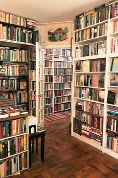 a room filled with lots of books on top of white shelves next to a wooden floor