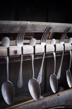 spoons and forks are hanging from an old metal rack