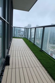 an empty balcony with grass growing on the floor and in between two windows, overlooking a cityscape