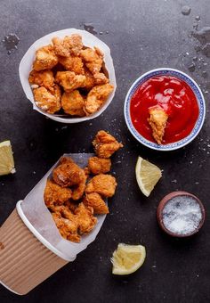 two bowls filled with fried food next to dipping sauce and lemon wedges on a table