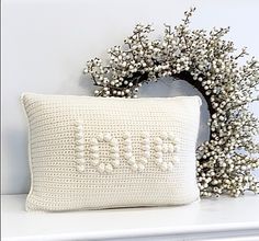 a crocheted pillow sitting on top of a white shelf next to a twig wreath