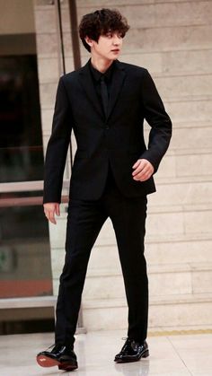 a young man in a black suit and tie standing on a red carpeted floor