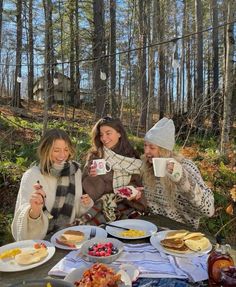 three women sitting at a picnic table with food