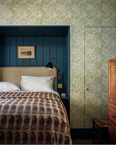 a bed sitting in a bedroom next to a wooden dresser and wall mounted lamp on top of it