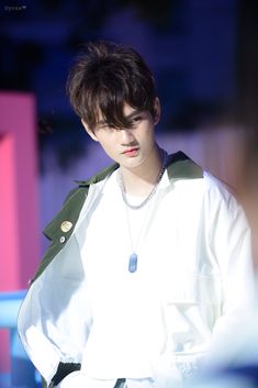 a young man wearing a white shirt and green jacket standing in front of a pink wall