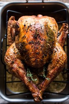 a roasted turkey in a roasting pan with herbs on the top and sides, ready to be cooked