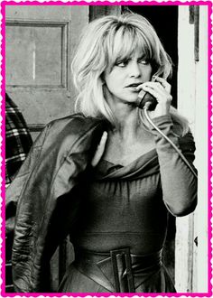 black and white photograph of woman talking on cell phone in front of door with man standing behind her