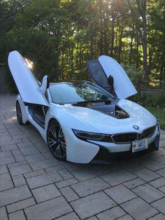 a white sports car with its doors open on a brick road in front of trees