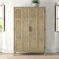 a tall wooden cabinet sitting next to two windows in a white room with wood flooring