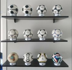 soccer balls are lined up on shelves in a room with white walls and black shelving