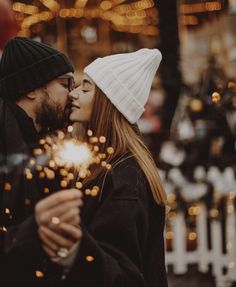 a man and woman kissing while holding sparklers in front of christmas lights on the street