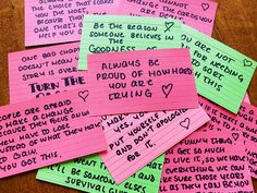 pink and green post it notes with writing on them sitting on a wooden table next to each other