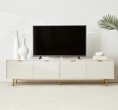 a flat screen tv sitting on top of a white cabinet next to vases and a potted plant