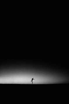 a lone person standing in the middle of a dark field with an airplane flying overhead