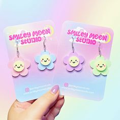 two pairs of smiley moon earrings are shown in front of a pink and blue background