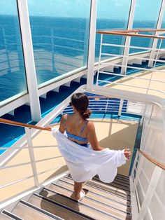 a woman in a white dress is walking up the stairs on a cruise ship looking out at the ocean