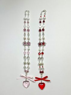 two necklaces with hearts, bows and pearls on white table top next to each other