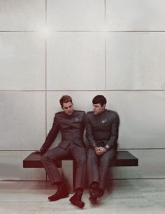 two men sitting on a bench in front of a wall, one wearing a suit