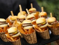 mini sandwiches with pickles and chips are on a black tray in front of other snacks