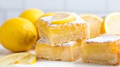 three lemon bars stacked on top of each other next to sliced lemons and two lemon wedges