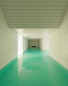 an empty room with green tiles on the floor and water in the pool at the end