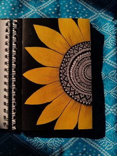 an open notebook with a yellow sunflower on the front and black cover, sitting on a blue patterned surface