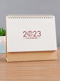 a desk calendar sitting on top of a wooden table next to a potted plant