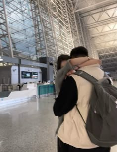 two people are standing in an airport with their backs to each other and one person is holding his backpack