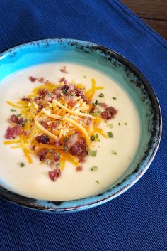 a bowl of soup with bacon, cheese and sour cream in it on a blue place mat