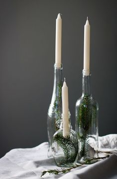 two glass bottles with candles in them sitting on a white table cloth next to each other