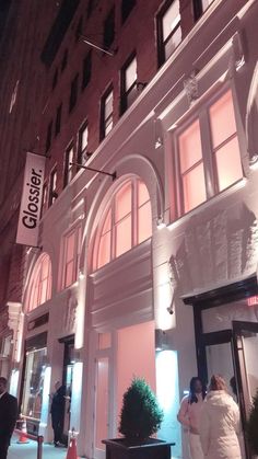 people are standing outside the entrance to a building at night with lights on and windows lit up