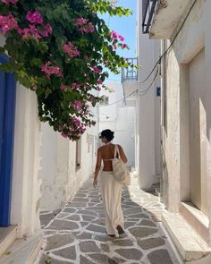 a woman walking down an alley way with pink flowers