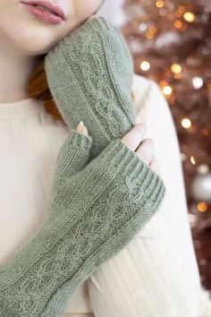 a woman wearing green knitted gloves next to a christmas tree