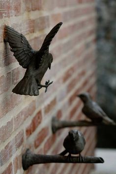 three metal birds are perched on the side of a brick wall