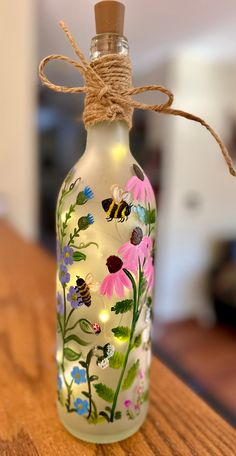 a glass bottle with flowers painted on it sitting on a wooden table next to a string