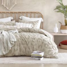 a bed with white and beige comforters in a bedroom next to a plant on the floor