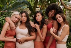 the models are posing together in front of some tropical plants and greenery, with their arms around each other's shoulders